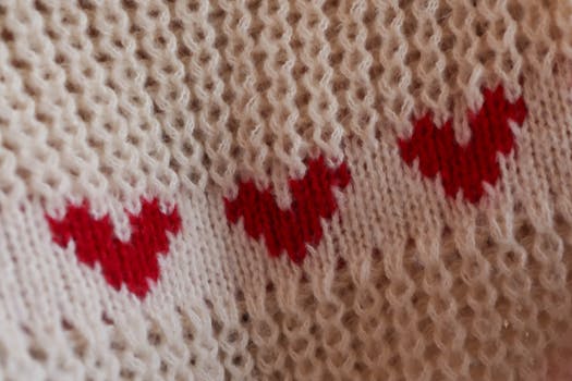 Close-up of a knitted fabric featuring red heart patterns on a soft beige background.